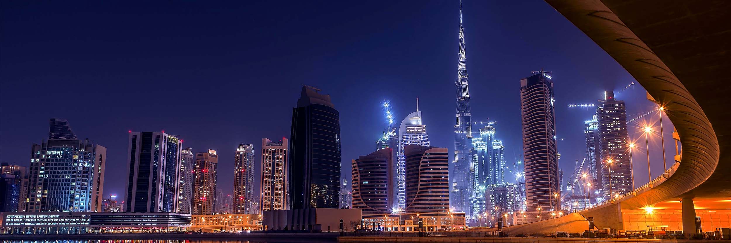 close up of Illuminated skyscrapers and Burj Khalifa reflecting on water under a clear night sky