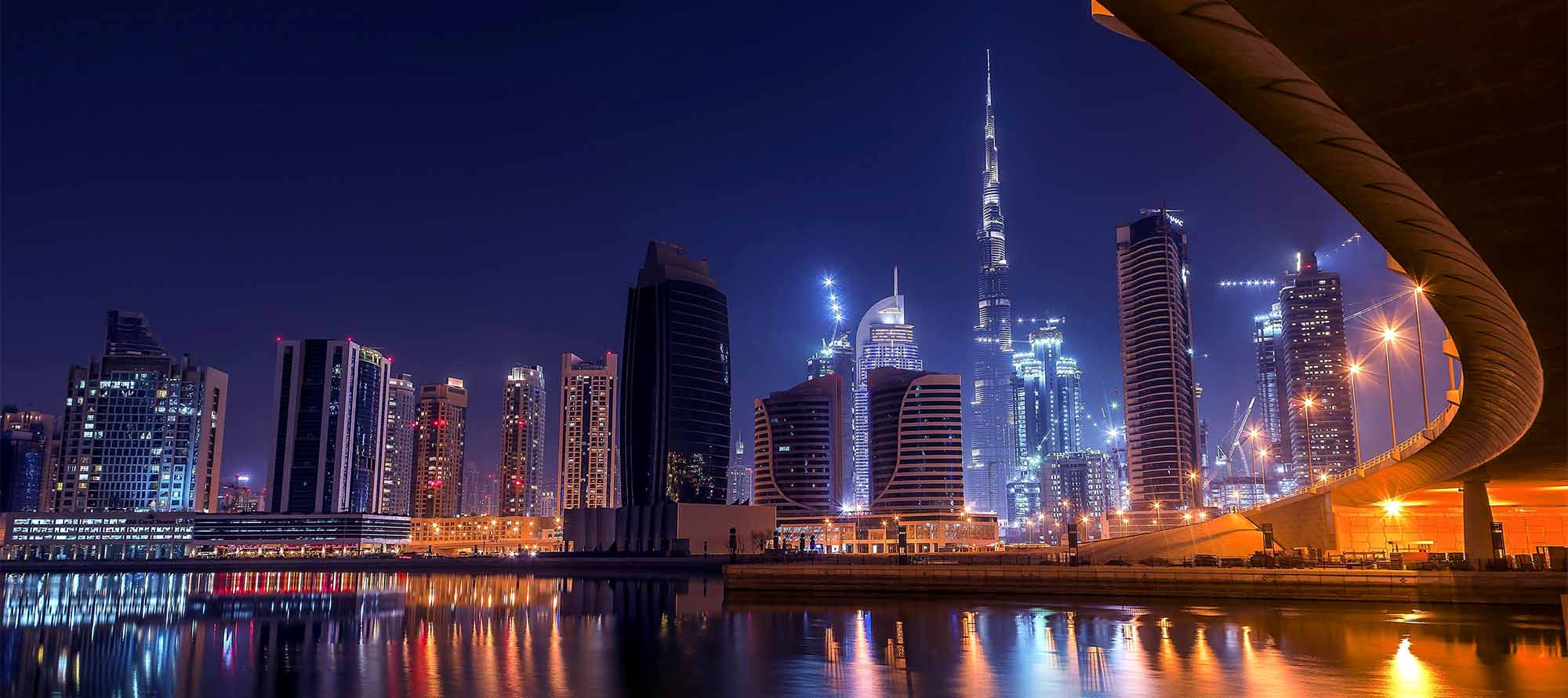 Illuminated skyscrapers and Burj Khalifa reflecting on water under a clear night sky