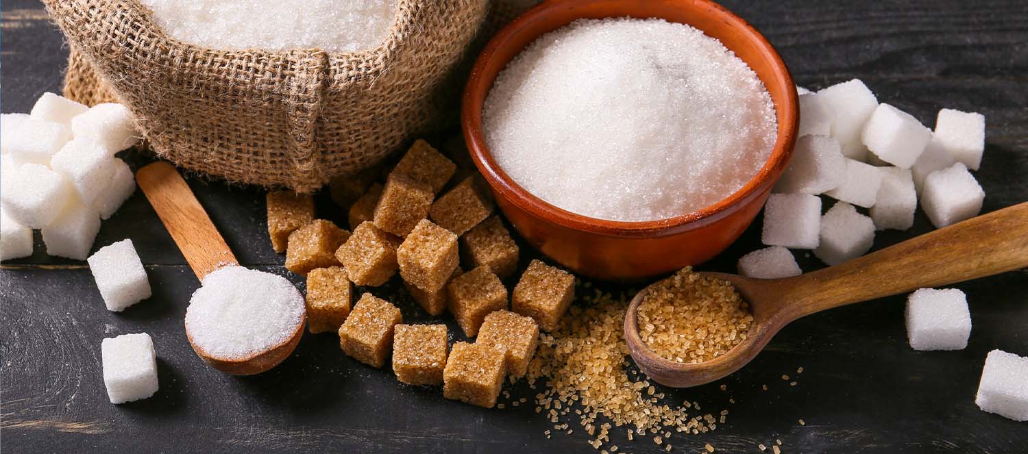 A bowl of white sugar and a pile of brown sugar cubes arranged on a dark surface.